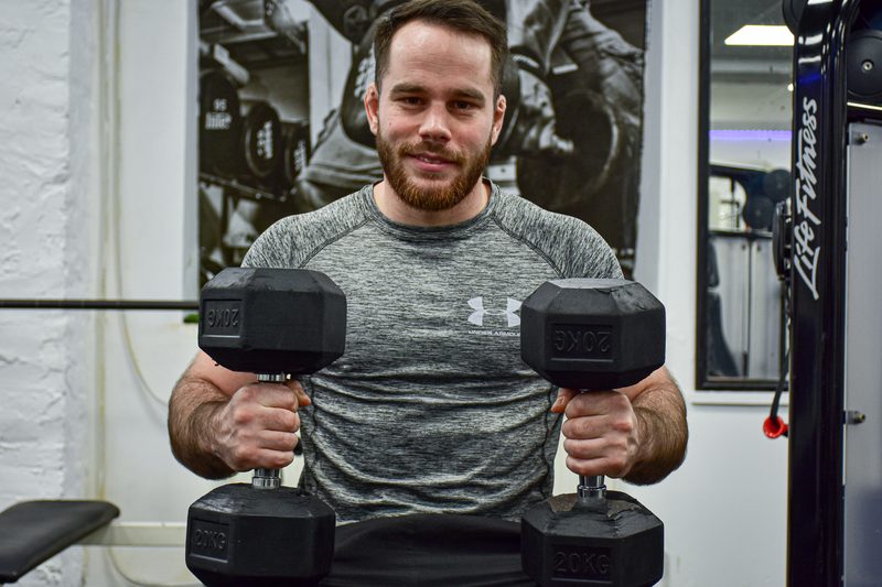 Levente Horváth, personal trainer, smiling while holding two dumbbells
